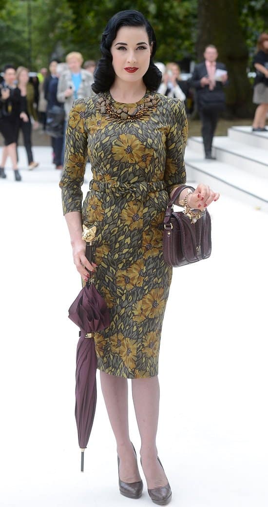 Dita von Teese carries a cat detailed maroon umbrella in a retro 50s vintage floral dress