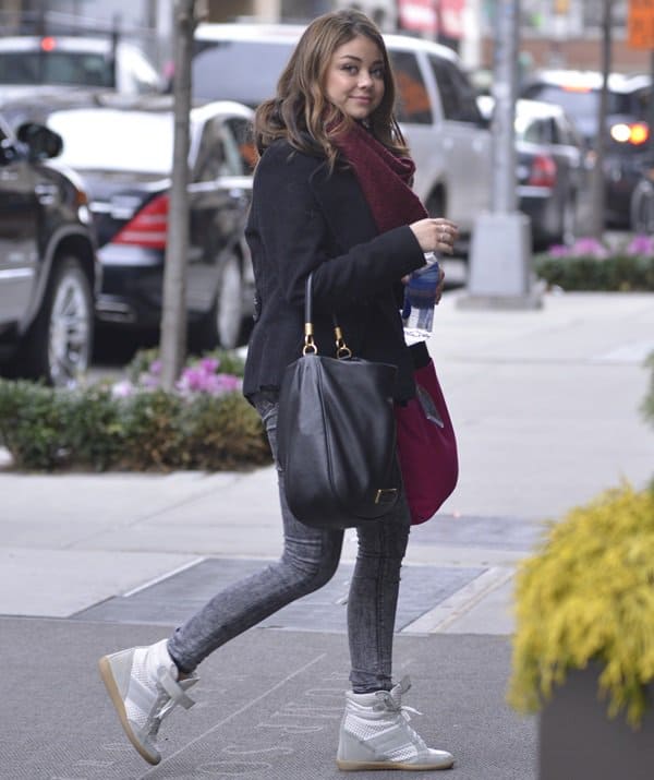 Sarah Hyland wearing a black pea coat, faded skinny jeans, and wedge sneakers